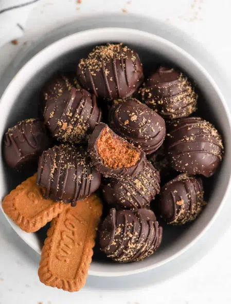 A plate of homemade Biscoff Truffles, coated in melted chocolate and sprinkled with crushed Biscoff cookies, on a rustic wooden table.