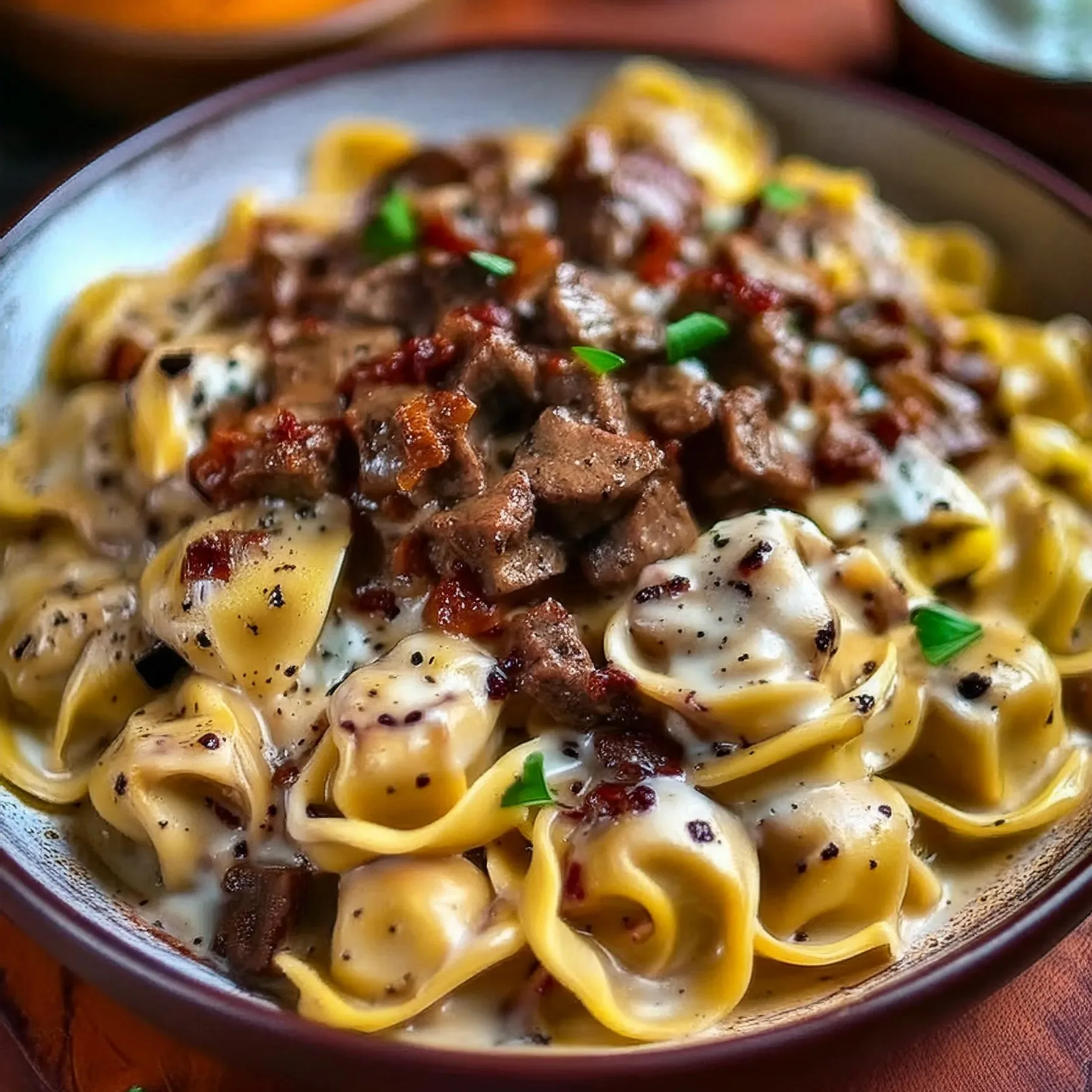 A bowl of Cheesesteak Tortellini smothered in rich provolone sauce, garnished with fresh herbs.